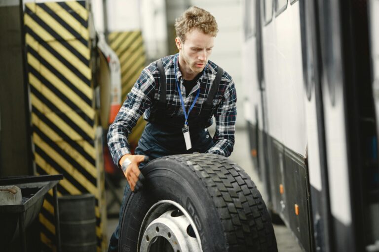 Auto mechanic working indoors in a vehicle repair garage managing a large tire.